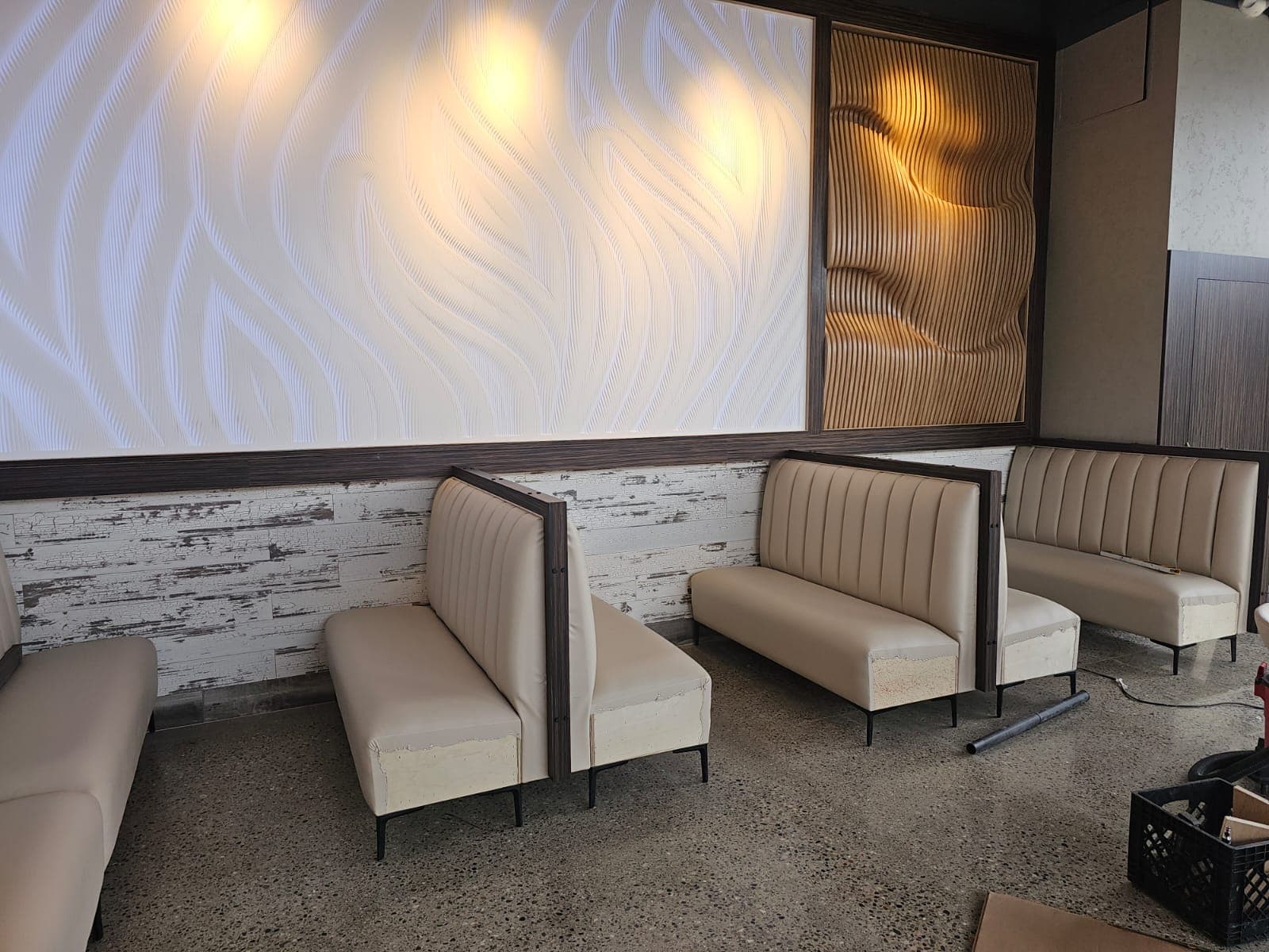 Cream-colored booths set against illuminated wavy textured wall panels in a modern restaurant.