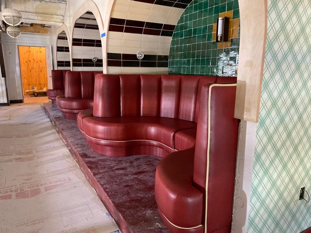 Curved red leather booths set in arched alcoves with green and black tiled walls.